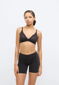 Μαύρο δαντελένιο σουτιέν με κυματιστά άκρα και ρυθμιζόμενους ιμάντες, σετ με ασύνορα μαύρα σορτς. Λείο, ελαστικό ύφασμα, μινιμαλιστικός σχεδιασμός.