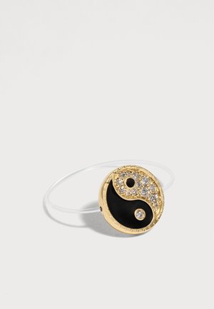 Bracelet en or avec un pendentif yin-yang rond ; une moitié en émail noir, l'autre moitié dorée avec des cristaux transparents, sur fond blanc.