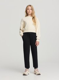 Felpa cropped color crema, pantaloni jogger neri con coulisse e sneakers beige con accenti rosa. Tessuto morbido, vestibilità comoda e design semplice.