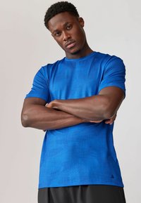 Blå atletisk T-shirt lavet af letvægtsmateriale med et struktureret geometrisk mønster. Korte ærmer og rund halsudskæring.