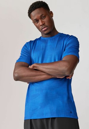 Blå atletisk T-shirt lavet af letvægtsmateriale med et struktureret geometrisk mønster. Korte ærmer og rund halsudskæring.