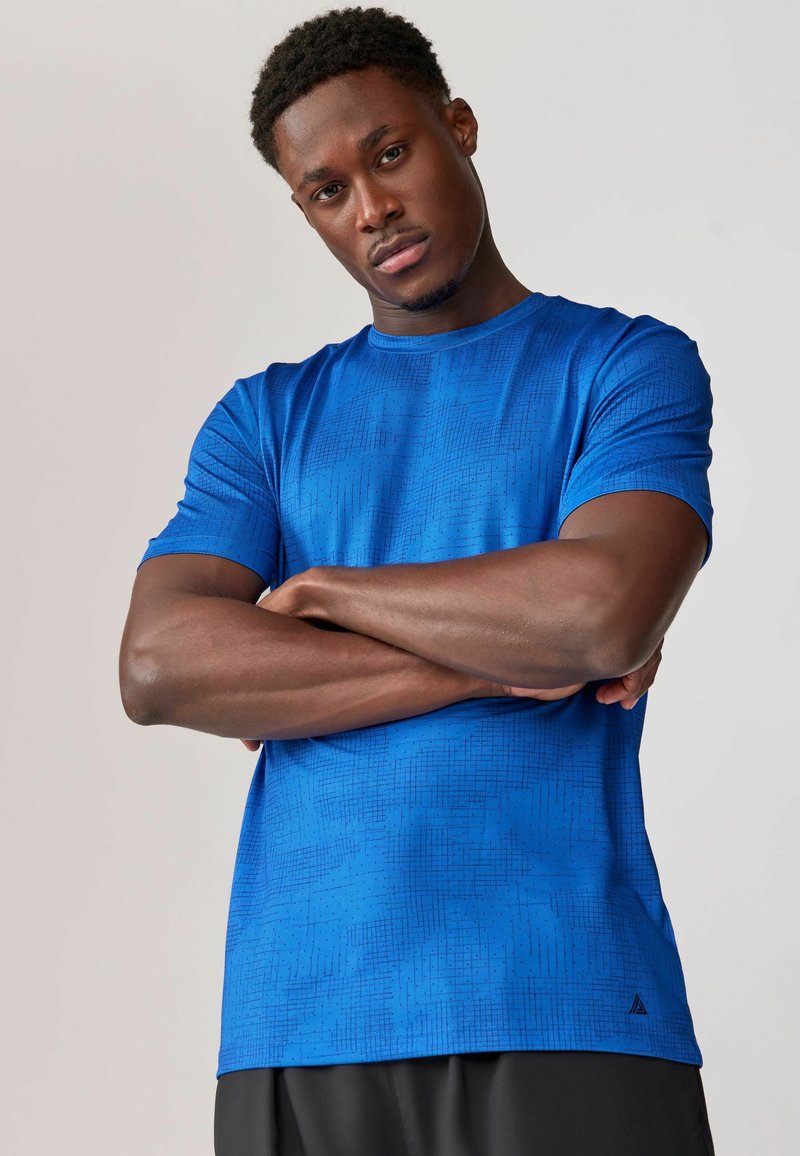 Blå atletisk T-shirt lavet af letvægtsmateriale med et struktureret geometrisk mønster. Korte ærmer og rund halsudskæring.