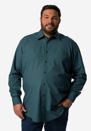 Camisa de manga larga de color verde azulado, confeccionada en tela suave, con un bolsillo en el pecho y botones negros, combinada con jeans azules.