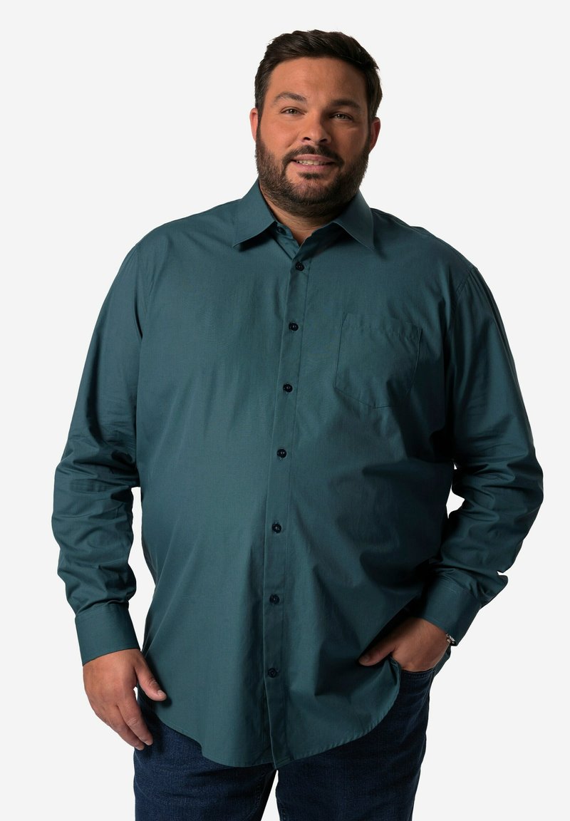 Camicia a maniche lunghe di colore verde scuro in tessuto morbido, con taschino sul petto e bottoni neri, abbinata a jeans blu.