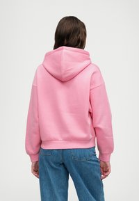 Rosa Kapuzenpullover mit lockerem Sitz, gerippten Bündchen und Saum. Der Hintergrund ist neutral und hebt die lebendige Farbe hervor.