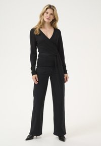 Pullover nero in maglia leggera, abbinato a jeans neri a vita alta e décolleté neri a punta. Design semplice con vita legata.
