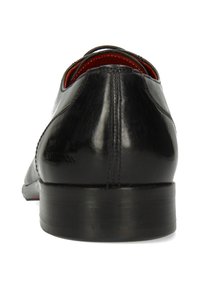 Scarpa in pelle nera vista dal retro, dotata di una texture liscia, tacco basso e dettagli di cucitura sottili. Fodera interna rossa visibile.