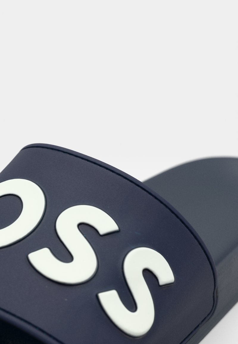 Nu-pied en bleu marine avec une large sangle arborant des lettres blanches en relief. Matériau lisse et durable au design moderne et minimal.