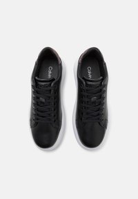 Pari mustia nahkakenkiä mustilla nauhoilla, valkoisilla pohjilla ja Calvin Kleinin brändillä kielessä ja sisäpohjassa, kuvattuna ylhäältä.