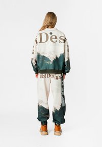 Conjunto de sudadera y pantalones de chándal de gran tamaño, con un estampado de montañas en tonos terrosos, con letras grandes y una etiqueta en los pantalones.