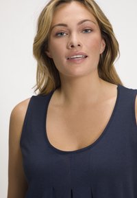 Top senza maniche blu navy realizzato in tessuto morbido, con scollatura a girocollo e pieghe centrali per texture e dettagli di design.