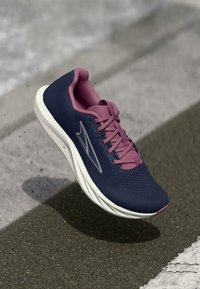 Tenniszcipő sötétkék hálós felsőrésszel és rózsaszín kiegészítőkkel, párnázott fehér talppel és textúrázott talppal a tapadás érdekében.