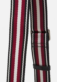 Cintura con strisce verticali in rosso, bianco e nero, caratterizzata da dettagli cuciti e una fibbia rettangolare in argento su uno sfondo semplice.