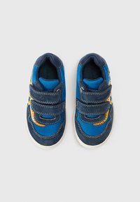 Zilas sporta kurpes ar tumszilām zamša detaļām, tīkliņa audumu, divām Velcro siksnām un spilgtu oranžu rakstu. Baltas gumijas zolītes. Plakans dizains.