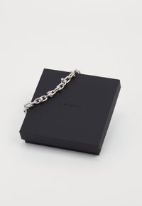 Caja de arce negro con una pulsera de cadena plateada gruesa colocada sobre la parte superior, sobre un fondo blanco.