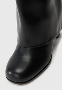 Black leather ankle boot with a rounded toe, smooth texture, and a slight heel. The design features a slouchy top that drapes softly.