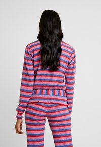 Dzianinowy komplet dwuczęściowy w różowo-czerwono-niebieskie paski. Charakteryzuje się prążkowaną fakturą i dopasowanym krojem z długimi rękawami oraz pasującymi spodniami.