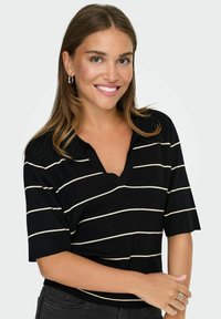 Young woman smiling, wearing a black short-sleeve top with white horizontal stripes, hoop earrings, and a silver ring on her right hand.
