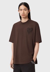 Brun oversized T-shirt i bomuld med korte ærmer, med et sort hjertegrafik på venstre brystområde. Simpelt, afslappet fit-design.