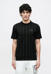 Czarny t-shirt wykonany z bawełny, z prążkowanym dekoltem typu crew, zdobiony tonowanym, powtarzającym się wzorem logo i krótkimi rękawami. Brak widocznych grafik ani akcentów.