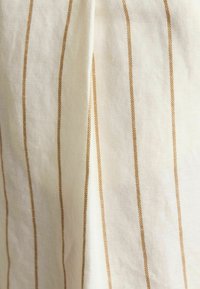 Beež ja kreemjas kangas, millel on vertikaalsed triibud. Tekstuur näib pehme ja kootud, triibulisel mustril on peen detailirohkus.