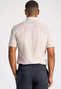 Camicia a maniche corte con motivo beige e un sottile design a scacchi, con colletto strutturato e vestibilità rilassata, indossata con pantaloni scuri.