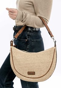 Sac en bandoulière en paille tressée de couleur beige avec une forme courbée, des accents en cuir brun et un fermoir en métal. Détails cousus le long des bords.