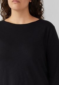 Zwart langekleurig shirt met lange mouwen, gemaakt van een zachte stof. Het heeft een brede halslijn en een ontspannen pasvorm met minimale zichtbare naden en zonder patronen.