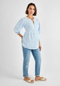 Blusa a righe blu e bianche con maniche a sbuffo, scollo a v e bordo in pizzo. Abbinata a jeans blu chiaro e scarpe beige slip-on.