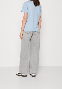 Lichtblauwe T-shirt met korte mouwen in combinatie met grijze wijde jeans. De jeans hebben gestikte accenten en worden gedragen met zwartgestreepte sneakers.