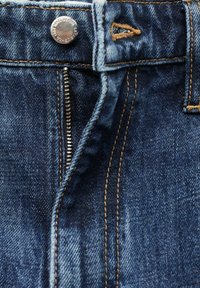 Jeans de mezclilla azul oscuro con costuras visibles, botón plateado y cremallera. Presenta un cierre tradicional y un lazo para cinturón en la cintura.