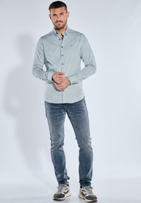 Hellegrünes, gemustertes Hemd mit langen Ärmeln, kombiniert mit blauen Jeans und grauen Sneakers mit weißen und beigen Akzenten.