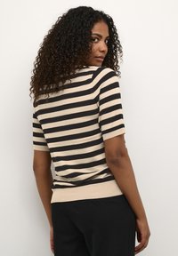 Pull �à manches courtes à rayures en beige et noir, avec une base côtelée, offrant une coupe ajustée et une texture douce. Détails comprenant un col rond.