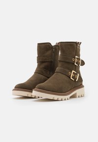 Bottines en daim marron avec deux brides et boucles dorées, dotées d'une semelle texturée et d'une plateforme couleur crème pour une meilleure adhérence.
