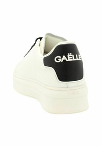 Sneaker bianca con finitura in pelle liscia, colletto imbottito e tab sul tallone nero con il logo “GAËLLE” in bianco. Suola spessa.