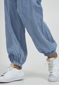 Pantalones sueltos de color azul claro con puños elásticos, hechos de un tejido suave, combinados con zapatillas blancas con un diseño texturizado y logotipo.