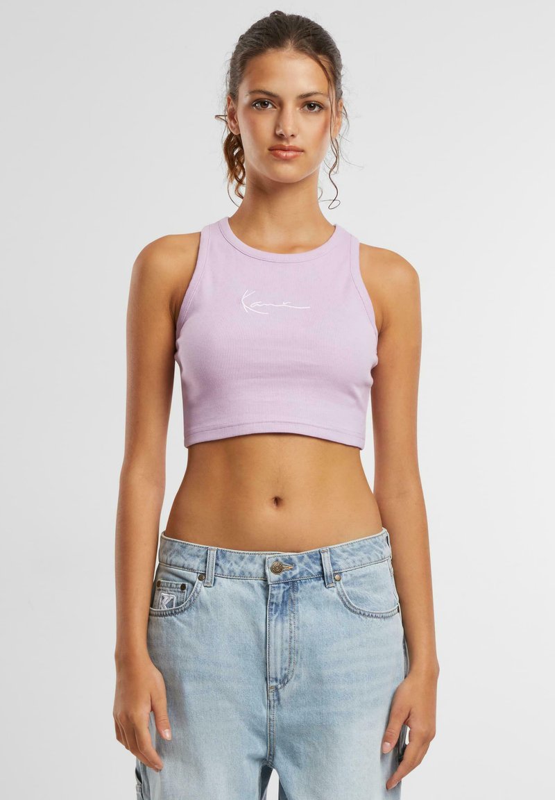 Lavendel avskåret tanktop med ribbestruktur, med en hvit skriptlogo på fronten; kombinert med lyseblå denimjeans.
