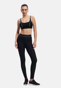 Czarny zestaw sportowy: staniczek i legginsy z białymi detalami. Gładki elastyczny materiał. Model w czarnych butach sportowych. Minimalistyczny design.