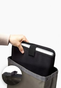 Borsa a tracolla grigia con una custodia nera per laptop parzialmente estratta. Tessuto spesso, bordi rinforzati, cinghia in Velcro, inserto circolare con dettaglio della borsa.