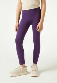 Paarse geribde leggings met een hoge tailleband. Draagt met beige gestructureerde sneakers, wat het strakke ontwerp en de levendige kleur benadrukt.