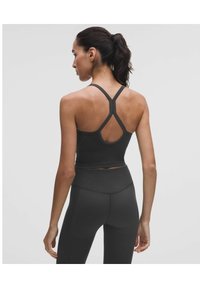 Fekete sportmelltartó keresztbe fonott hátrészes dizájnnal, rugalmas anyagból készült. Magas derekú fekete leggingshez párosítva, bordázott textúrával.