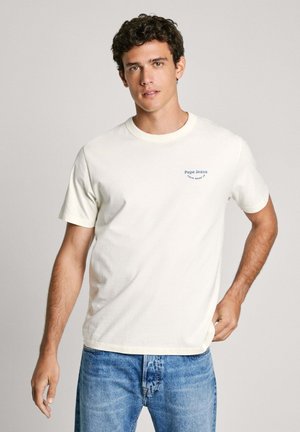Krem majica od pamuka s kratkim rukavima, okruglim izrezom i plavim "Pepe Jeans" logom sa lijeve strane. Nosena s svijetloplavim trapericama.