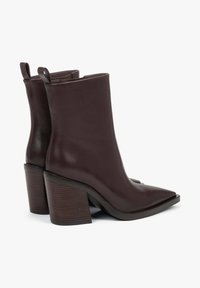 Brązowe skórzane botki za kostkę z ostrym szpicem, obcasem typu bloczek i gładką fakturą. Wyposażone w subtelne uchwyty ułatwiające zakładanie.