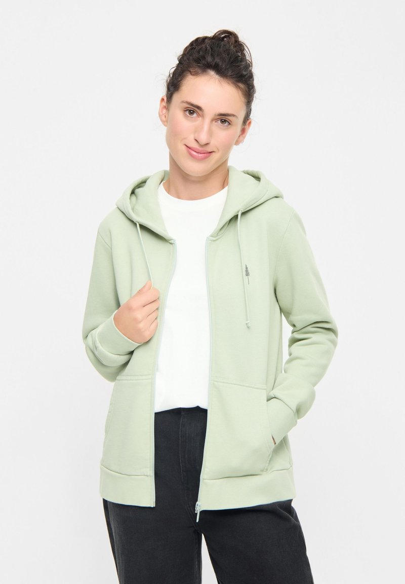 Felpa con zip verde chiaro realizzata in tessuto morbido, caratterizzata da un cappuccio con cordino, tasche frontali e un piccolo logo ad albero sul petto.
