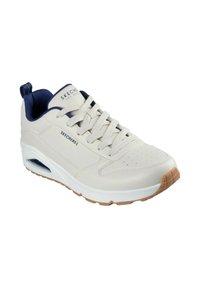 Zapatilla blanca con upper de cuero suave, acentos en color marino y una suela acolchada. Presenta perforaciones en la puntera y una suela de goma texturizada.