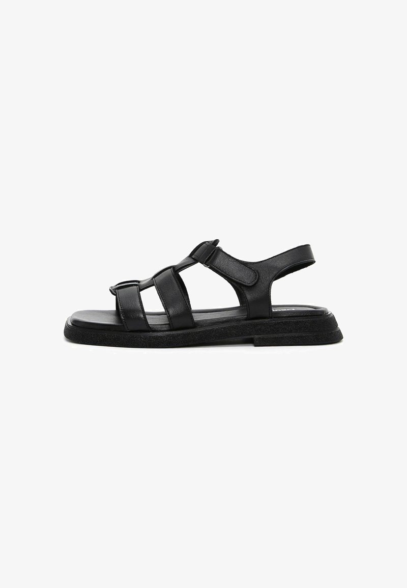 Sandale plate en cuir noir avec des brides réglables et une semelle rembourrée, conçue pour un usage décontracté et le confort.