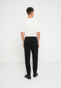 Tricou alb din bumbac cu guler rotund, asortat cu pantaloni de trening negri, conici, cu un tiv elastic la talie și la manșete. Pantofi negri fără șireturi.