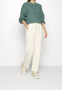 En petrolblå stickad tröja med vid halsringning och puffärmar, i kombination med krämfärgade byxor med hög midja och ljusa sneakers.