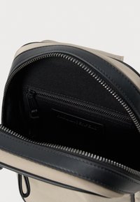 Beige vászontáska belseje fekete cipzárral záródik. Tartalmaz egy kis cipzáras zsebet és fekete textilbélést.