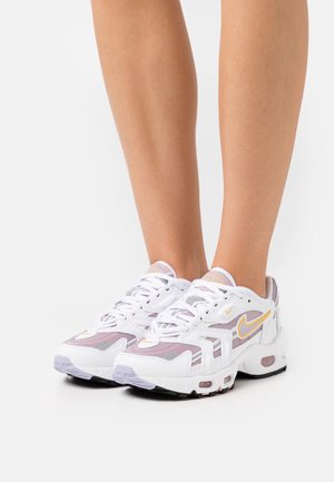 Witte sportieve sneakers hebben een bovenwerk van mesh met paarse accenten, een vetersluiting en een contrasterende zwarte zool. Opvallend merkembleem zichtbaar.